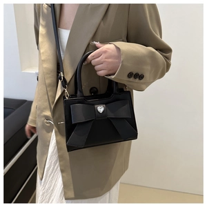 Dettaglio della borsa nera con fiocco, cristallo a cuore e tracolla su una modella