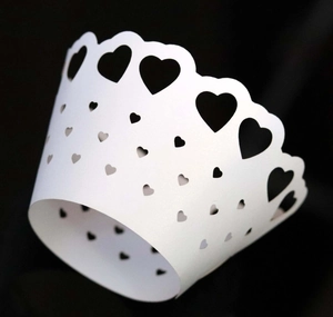 Detail of white laser-cut cupcake wrappers with intricate heart patterns for wedding decor