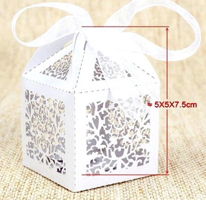 Close-up of white laser-cut wedding favor box with heart patterns and white silk ribbon
