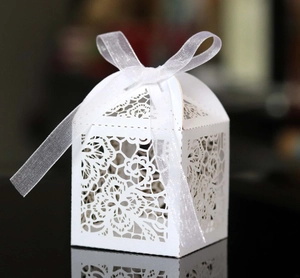 Macro view of white laser cut wedding candy box with elegant floral hollow pattern and ribbon