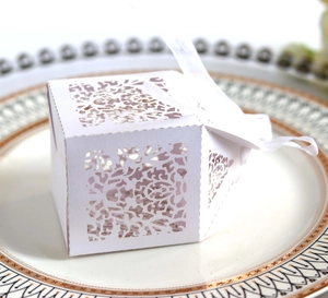 Macro shot of white laser-cut wedding favor box with floral patterns and ribbon