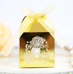 Close-up of laser-cut gold mirror wedding favor box with floral patterns and a silk ribbon