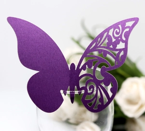 Close-up of purple laser-cut butterfly card on glass rim for wedding table decor