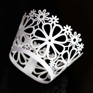 Macro shot of laser-cut white pearl paper cupcake wrappers with intricate daisy patterns
