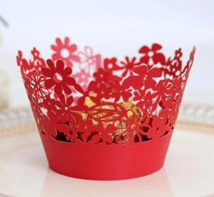 Intricate laser-cut red paper cupcake wrapper with floral hollow pattern and gold candy