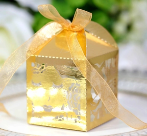 Détail d'une boîte cadeau dorée ajourée avec motif rose découpé au laser et ruban satin
