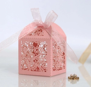 Detail of pink laser-cut wedding favor box with intricate rose patterns and pink ribbon