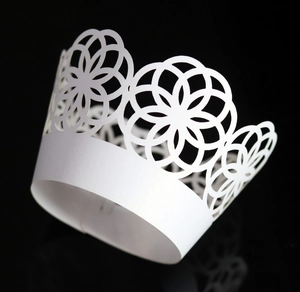 Macro view of laser-cut white pearlescent paper cupcake wrappers with crown flower patterns