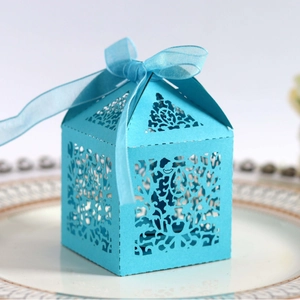 Teal laser-cut wedding favor box with floral patterns and silk ribbon on a plate