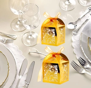 Detail of laser-cut hollow floral gold gift boxes with orange silk ribbon on a dinner table