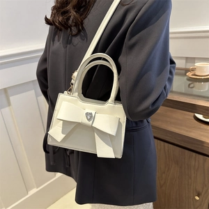 Mini borsa a mano bianca con fiocco e cristallo a cuore su un abito grigio