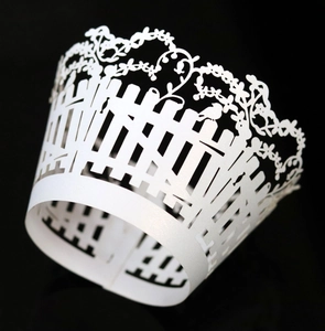 Macro view of white laser-cut floral and bird cupcake wrapper with fence pattern