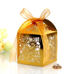 Close-up of golden laser-cut floral wedding favor box with an orange organza ribbon bow