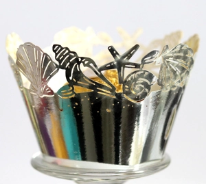 Macro detail of laser-cut silver cupcake wrapper with ocean shell and starfish patterns
