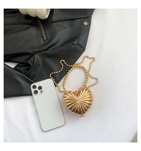 Macro detail of golden heart bag with radial texture and pearl chain next to a phone