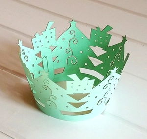 Laser-cut Christmas tree cupcake liners in light green on a white wooden background