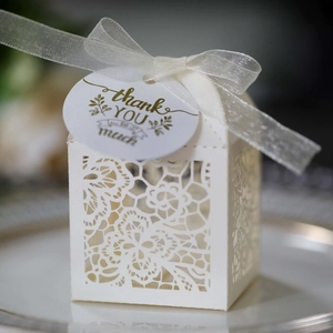 Detail view of white laser-cut floral wedding favor box with ribbon and thank you tag