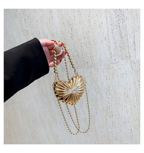 Detail of a gold heart-shaped metal handbag with radiating texture and pearl chains