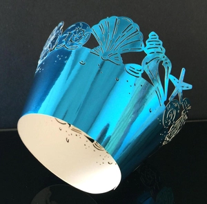 Macro detail of laser-cut metallic blue cupcake wrapper with sea shells and starfish design