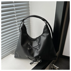 Detail of a black hobo bag with a lace-up decorative bow and silver metal eyelets