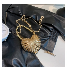 Detail of gold heart-shaped evening bag with metallic texture on a black leather jacket