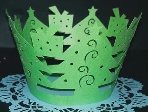 Detail of green laser-cut Christmas tree cupcake wrapper with festive hollow patterns