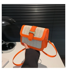 Close-up of golden H buckle on a woven straw and orange leather crossbody handbag