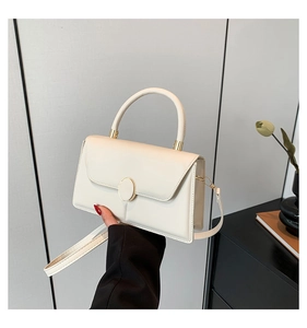Detail of elegant cream handbag with gold twist-lock and structured top handle design