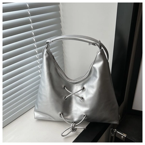 Detail of silver metallic hobo bag featuring lace-up design and metal eyelets on a windowsill