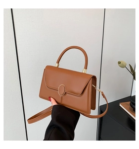 Detail view of brown leather handbag featuring gold metal buckle and sturdy top handle