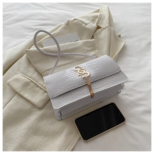 Close-up of beige crocodile pattern bag with gold letter clasp and chain tassels