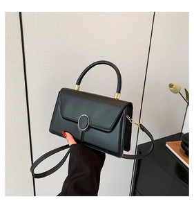 Detail shot of black rectangular handbag with a distinctive gold round metal buckle closure