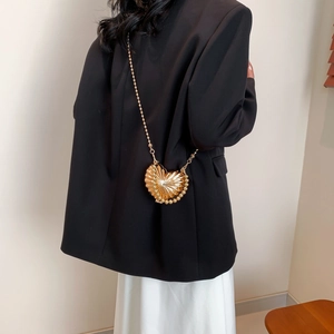 Golden heart-shaped metal crossbody bag with pearl trim and chain strap on a black blazer