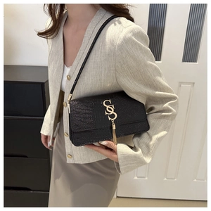 Detail of black croc-effect crossbody bag with gold SS logo and tassel on beige blazer