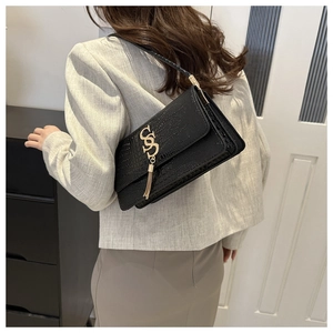 Close-up of black crocodile pattern shoulder bag with gold metal logo and long tassel
