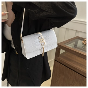 Detail of white crocodile pattern flap bag with gold S-shaped buckle and tassel charm