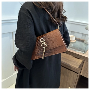 Detail of brown crocodile pattern shoulder bag featuring gold logo and tassel accent