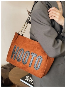 Detail of brown faux suede tote bag with HOOTO lettering and gold chain strap close-up