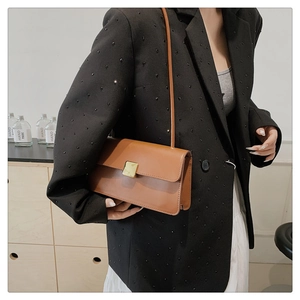 Borsa a tracolla in pelle marrone con fibbia dorata indossata su un completo formale chic