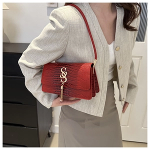 Detail of red croc-embossed shoulder bag with golden S-clasp and fringe chain