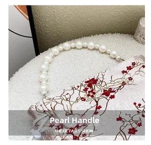Detailed view of pearl handle and red plum flower embroidery on white shoulder bag