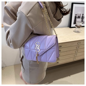 Detail of purple quilted shoulder bag with gold chain strap and stylish tassel pendant