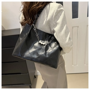 Detail of black quilted tote bag with silver chain strap and three pearl accents