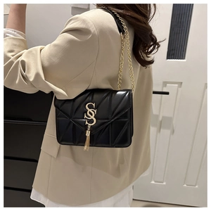 Close-up of black quilted shoulder bag featuring gold S logo, tassel, and chain strap