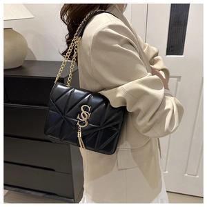 Close-up of black quilted shoulder bag with gold hardware and tassel detail on beige blazer