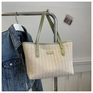 Détail du cabas en paille tressée avec bordure en cuir vert clair et logo de la marque