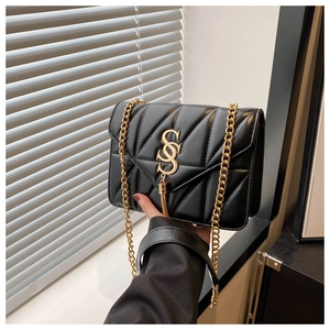 Detail of black quilted leather shoulder bag with golden S-logo and metal tassel accent