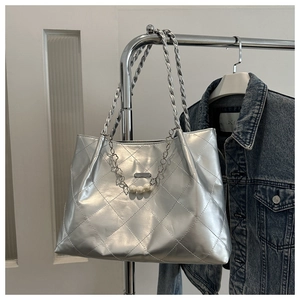 Macro detail of quilted silver metallic tote bag with pearl chain and flower charm