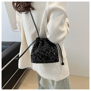 Detail of a sparkling black sequined bucket bag shown on a model in a minimalist setting