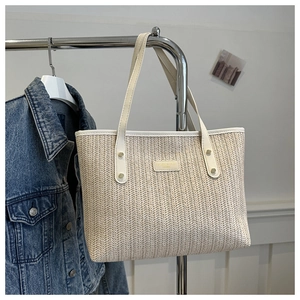 Détail du sac cabas en paille beige avec poignées en cuir blanc et rivets dorés